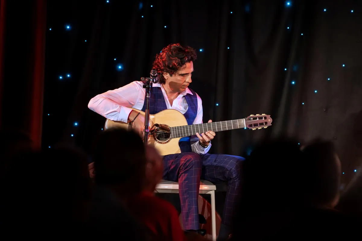 Ernesto Castillo playing solo guitar in front of a starry curtain