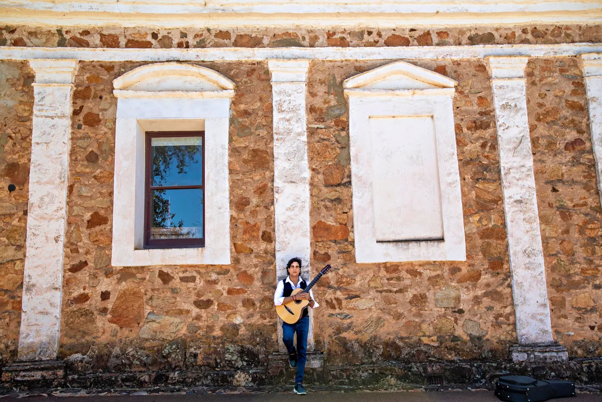 Ernesto Castillo with guitar against a stone heritage wall