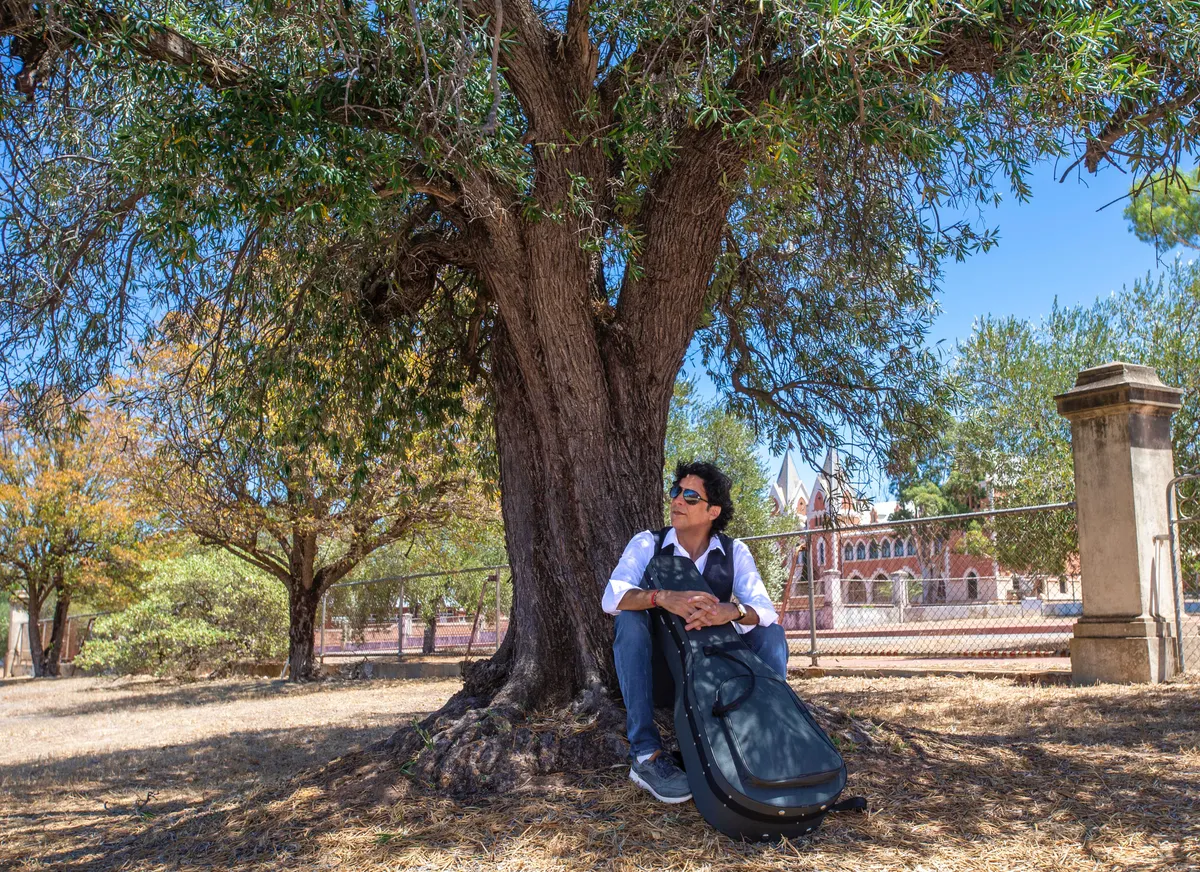 Ernesto Castillo resting under a large tree with his guitar