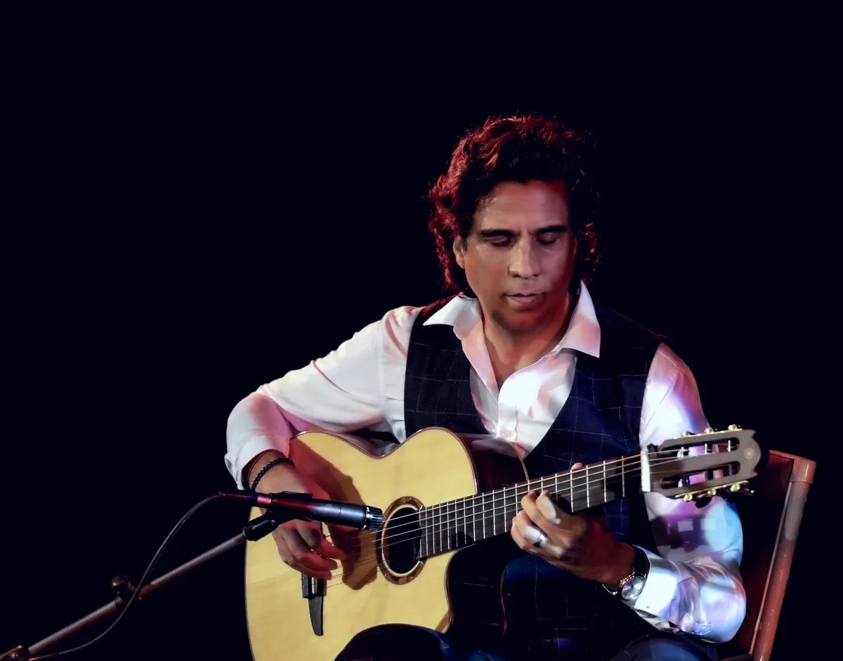 Ernesto Castillo playing nylon-string guitar on a dark stage
